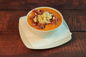 A bowl of soup with bacon and cheese on top. The bowl is on a white napkin