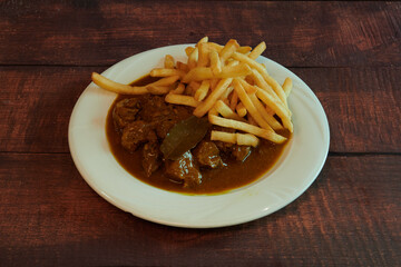 A plate of food with a piece of meat and french fries. The meat is covered in gravy and the fries are golden brown
