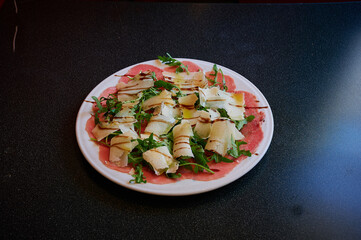 A plate of food with a white plate and a black table. The food is a salad with cheese and spinach