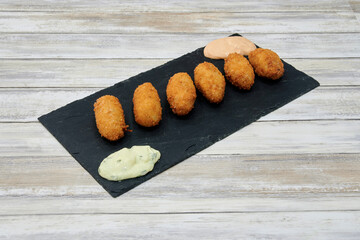 A plate of fried food with a dipping sauce. The food is small and round. There are six pieces of food on the plate