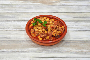 A bowl of food with meat and chickpeas. The bowl is red and white. The food is on a wooden table