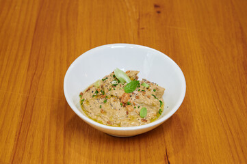 A bowl of food with a green leaf on top. The bowl is white and the food is brown