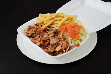 A plate of food with a piece of meat and a side of fries. The meat is cut into small pieces and the fries are golden brown. There is also a salad on the plate