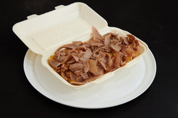 A container of meat with a white lid on a plate. The container is white and has the word 