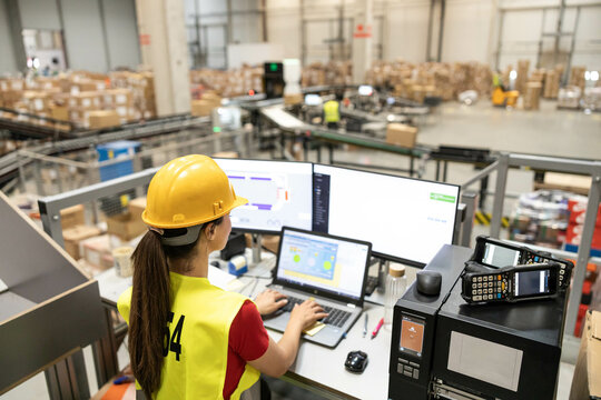 A focused employee monitors operations on multiple screens in a warehouse, emphasizing technology in logistics.