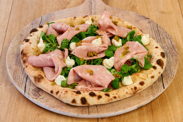 A pizza with ham and spinach on top. The pizza is on a wooden board. The crust is brown and the toppings are spread out