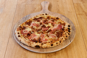 A pizza with ham and onions on a wooden board. The pizza is brown and has a crust