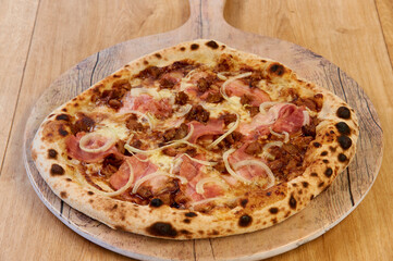 A pizza with ham and onions on top. It is sitting on a wooden board. The pizza is brown and has a crispy crust