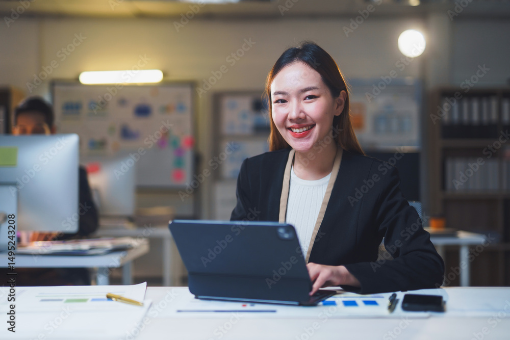 Poster young manager working late at her modern office, smiling happily while using advanced technology on 