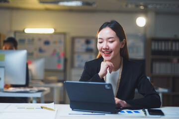 Young manager working late at night, smiling while using a tablet in a modern office, embodying professionalism and dedication