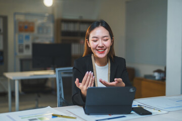 Young manager smiling and gesturing during a video conference on a tablet in her office at night