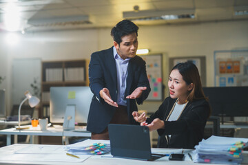 Businessman and businesswoman arguing over project details while working late in an office, facing stress and pressure from looming deadlines