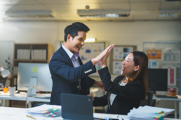 Two smiling business professionals celebrating successful teamwork with a high five in a modern office setting, radiating enthusiasm and unity