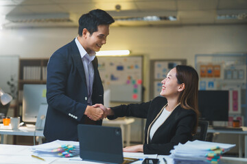 Two Asian businesspeople shaking hands in a modern office, celebrating a successful deal and marking the beginning of a promising partnership