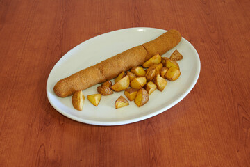 A plate of food with a long piece of food on it and some potatoes. The plate is on a wooden table