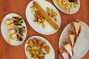 A table with a variety of food items including a plate of chicken wings, a plate of potato wedges, a plate of salad, and a plate of meat