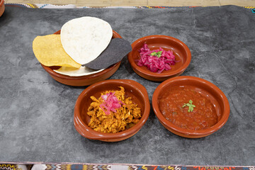 A plate of food with a bowl of meat and a bowl of sauce. There are also some tortilla chips on the plate