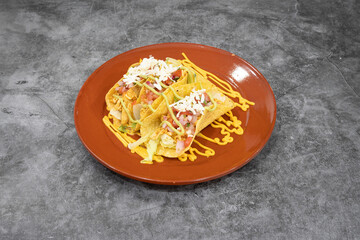 A plate of two tacos with cheese and lettuce on top. The plate is on a grey counter