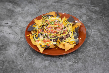 A plate of nachos with cheese and sour cream. The nachos are topped with tomatoes, onions, and green sauce