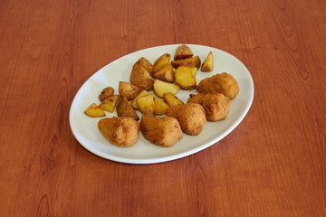 A plate of fried chicken and potatoes. The chicken is cut into small pieces and the potatoes are cut into cubes