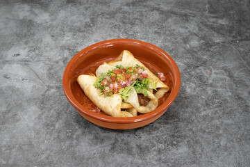 A bowl of food with three tortillas in it. The tortillas are covered in salsa and topped with lettuce