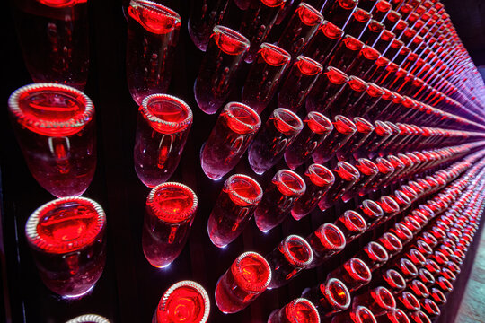 Rows of red wine bottles stored upside down in a modern wine cellar, illuminated with artistic lighting to create a striking visual effect
