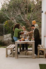 Group of four friends standing at a table and putting food on plates, outdoors