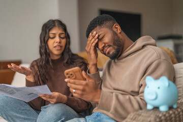 Couple discussing finances while sitting on the couch with documents and a piggy bank nearby in a...