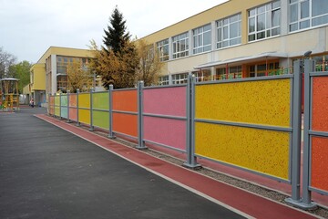Naklejka premium Colorful fence surrounding a school playground with vibrant panels and a backdrop of classrooms