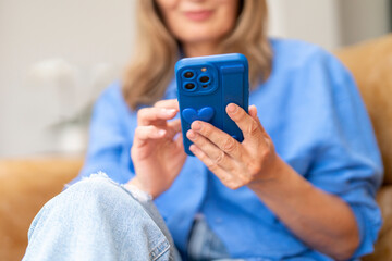 Woman using smartphone while sitting comfortably in a cozy living room with casual attire and a...