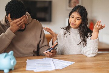 Couple discussing financial issues at home while reviewing bills and using a calculator in a cozy kitchen setting