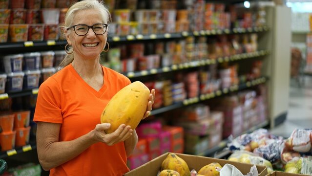 Closeup portrait of smiling happy pretty mature woman selecting a papaya fruit in a grocery store.