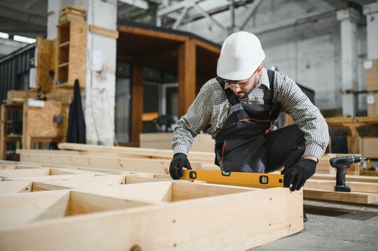 Carpenter checking level of wooden frame in workshop for modular house production