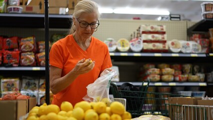 Slow motion portrait of smiling happy pretty mature woman selecting lemons in a grocery store.