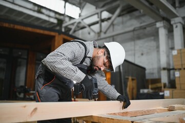 Carpenter using cordless drill assembling wooden frame in workshop