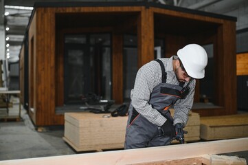 Carpenter working on wooden plank for modular house production in construction workshop