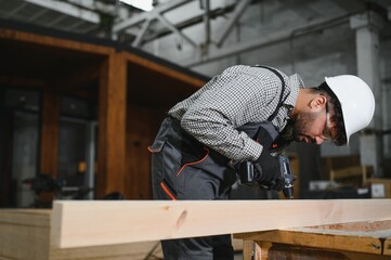 Carpenter using cordless drill on wooden plank in workshop