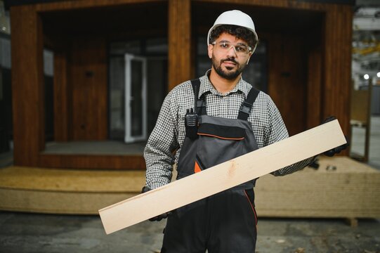 Construction worker holding wooden plank in modular house production workshop