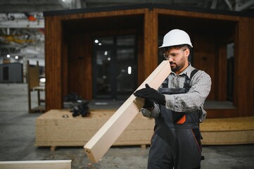 Construction worker carrying wooden plank for modular house production