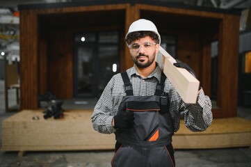 Arab construction worker carrying wooden plank in prefabricated house workshop