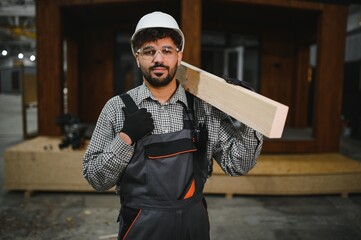 Construction worker carrying wooden plank in workshop for modular housing production