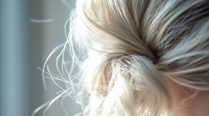 Naklejka premium Close up of soft blonde hair styled in a loose bun with natural light illuminating delicate strands
