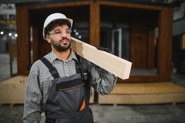 Construction worker carrying wooden plank in modular house factory