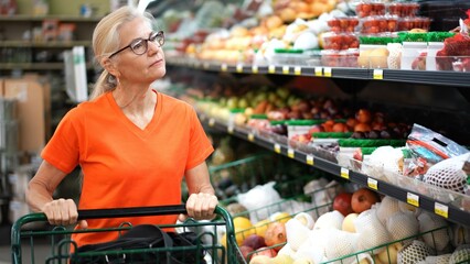 Closeup portrait of happy pretty mature woman pushing a shopping cart in a grocery store.