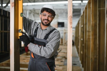Construction worker using spirit level on wooden beam in workshop