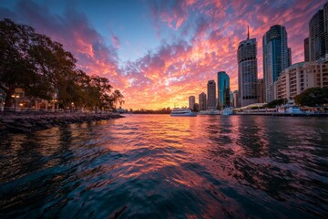 Fototapeta premium Vibrant sunset over a river with city skyline and colorful clouds reflecting on the water