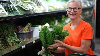 Closeup portrait of smiling happy pretty mature woman selecting a swiss chard or silverbeet leafy...