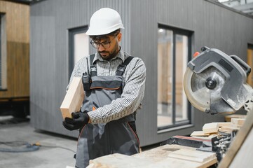 Arab carpenter examining wooden plank in prefabricated house workshop