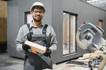 Arab carpenter holding wooden plank in modular house production workshop