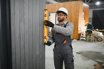 Construction worker using spirit level on modular house wall panel
